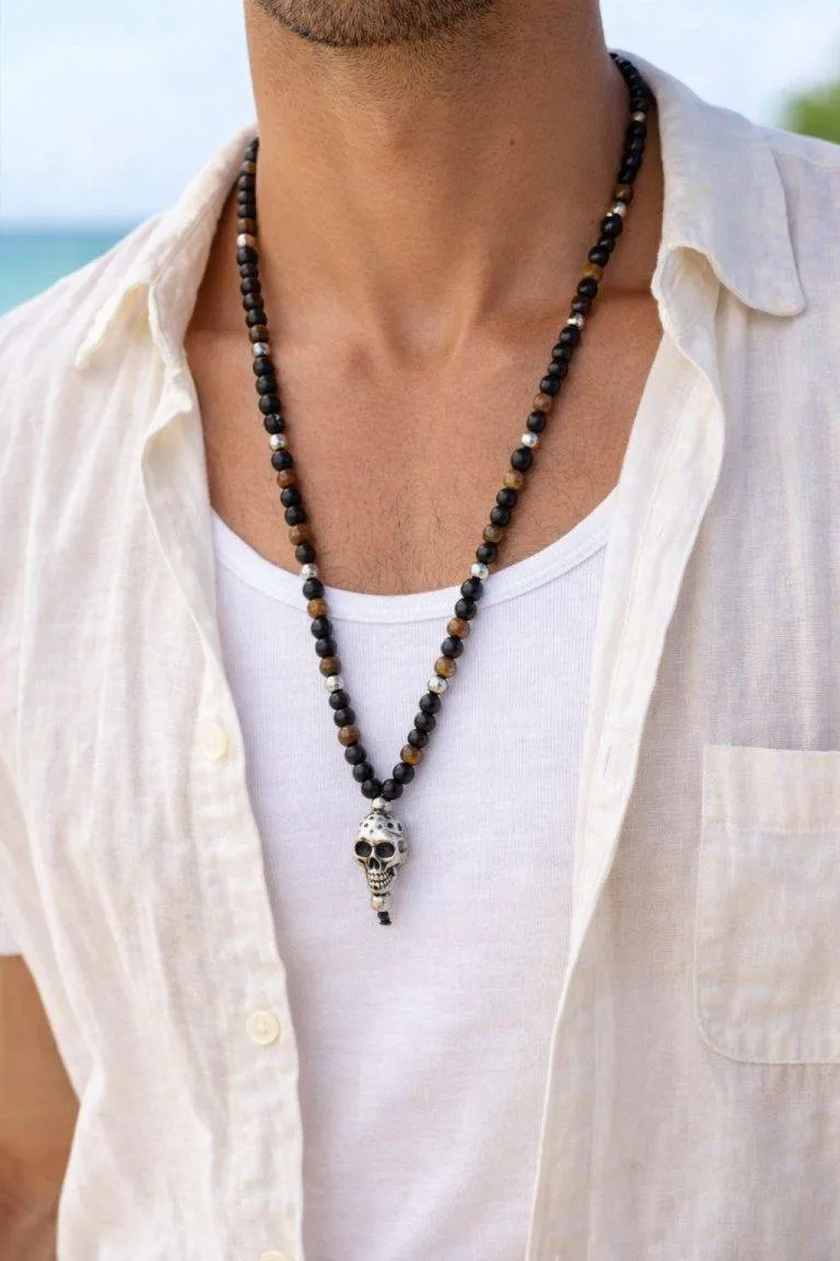 Das Model trägt ein weißes Hemd und ein Tank-Top und präsentiert die Rebel Skull Steinkette mit einem auffälligen Totenkopf-Anhänger aus Metall - ein auffälliges Statement.